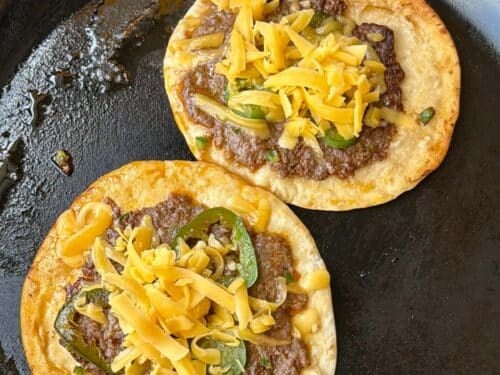 Flipped smashed tacos topped with shredded cheddar melting in the skillet