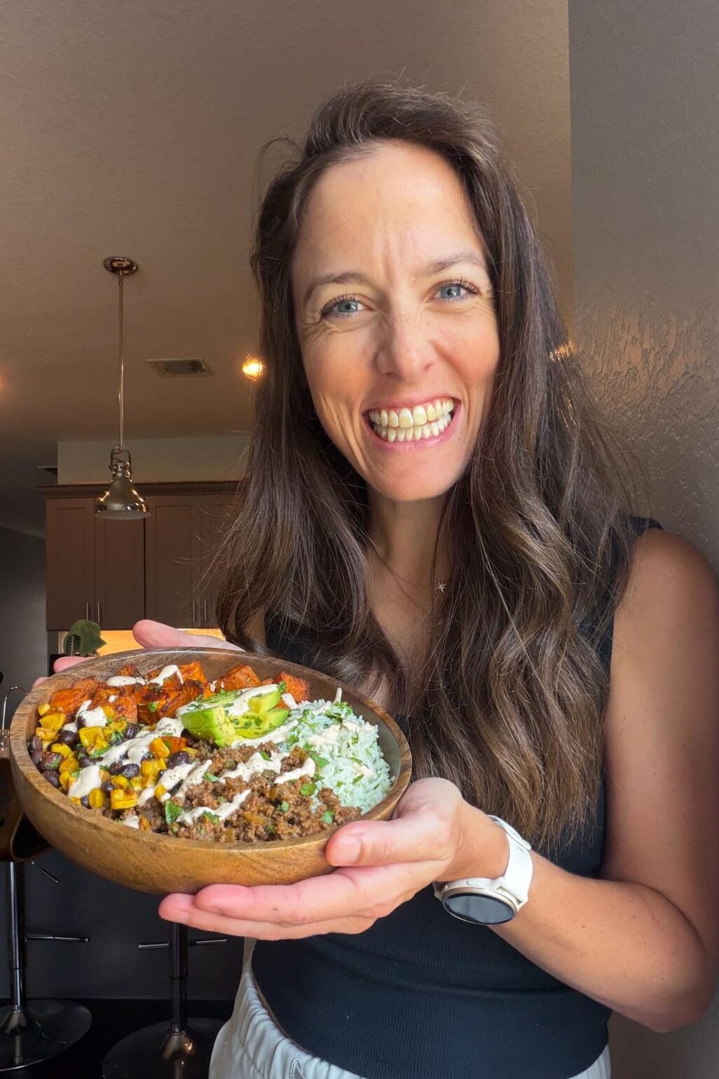 London Lea holding a bowl of sweet potato taco bowls with ground beef and chipotle crema in her kitchen.