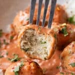 A fork lifting a tender baked butter chicken meatball out of a silky butter chicken sauce.