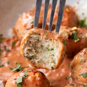 A fork lifting a tender baked butter chicken meatball out of a silky butter chicken sauce.