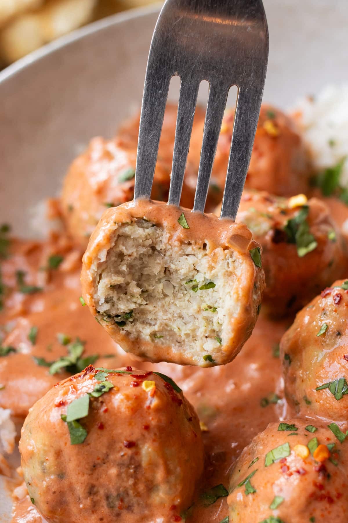 Fork lifting a tender baked chicken meatball out of silky butter chicken sauce