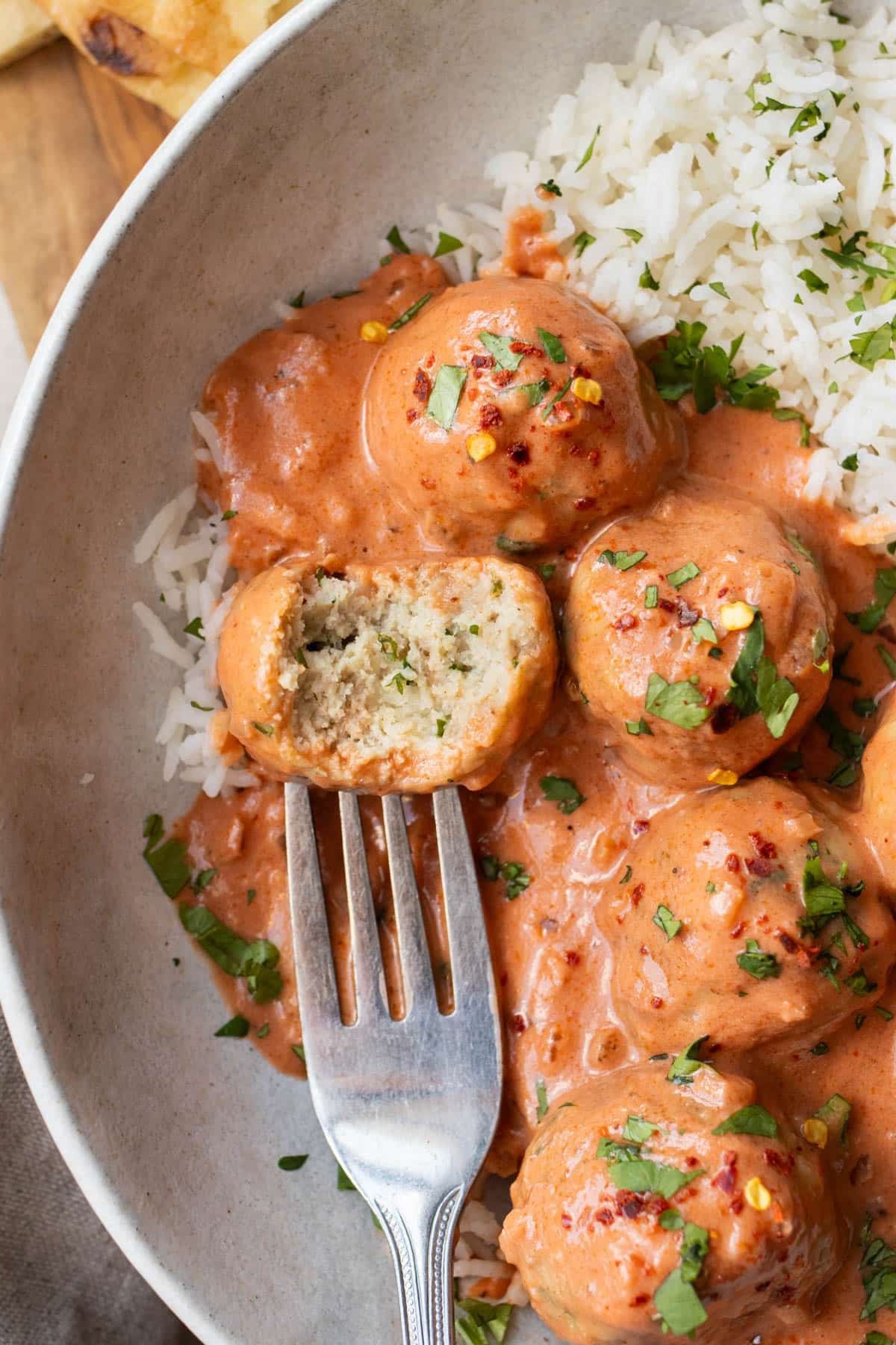 Plate of creamy butter chicken meatballs over basmati rice with a meatball cut open to show the tender center