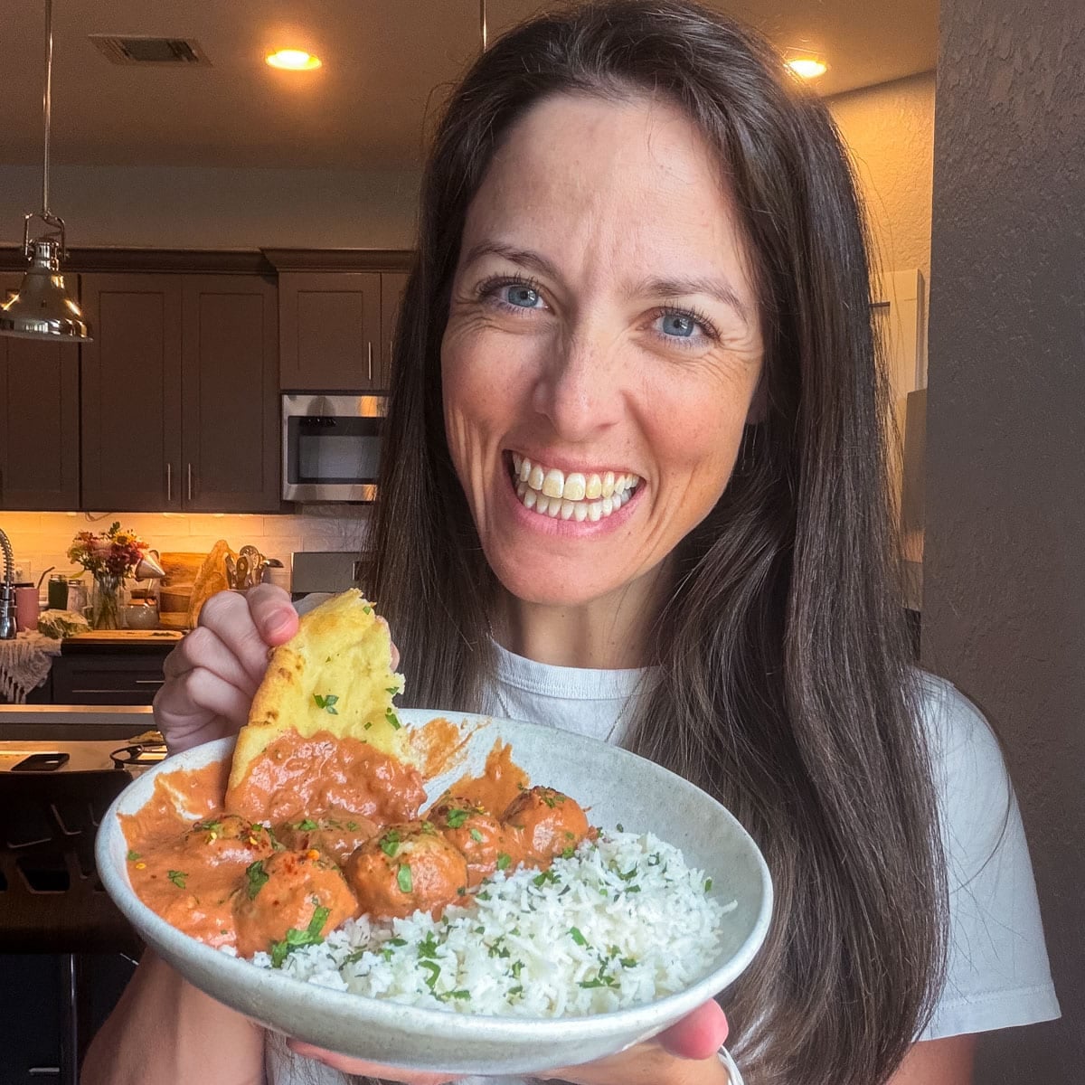 London Lea holding a plate of butter chicken meatballs with basmati rice and naan in her Austin kitchen.