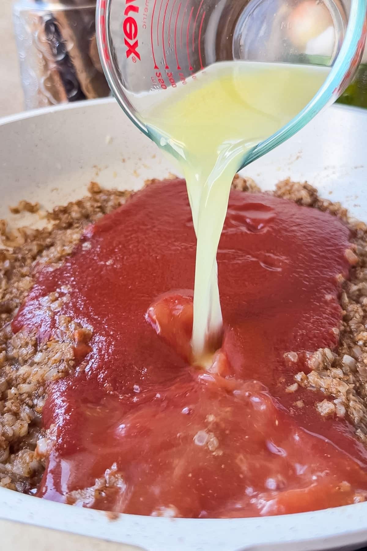 Chicken broth pouring into tomato sauce in a skillet for an easy butter chicken sauce