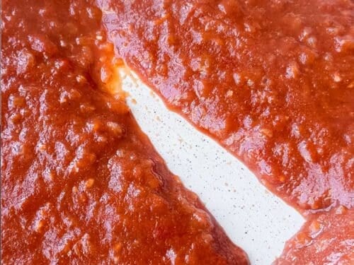 Thickened tomato sauce with a spoon trail across the skillet for butter chicken meatballs