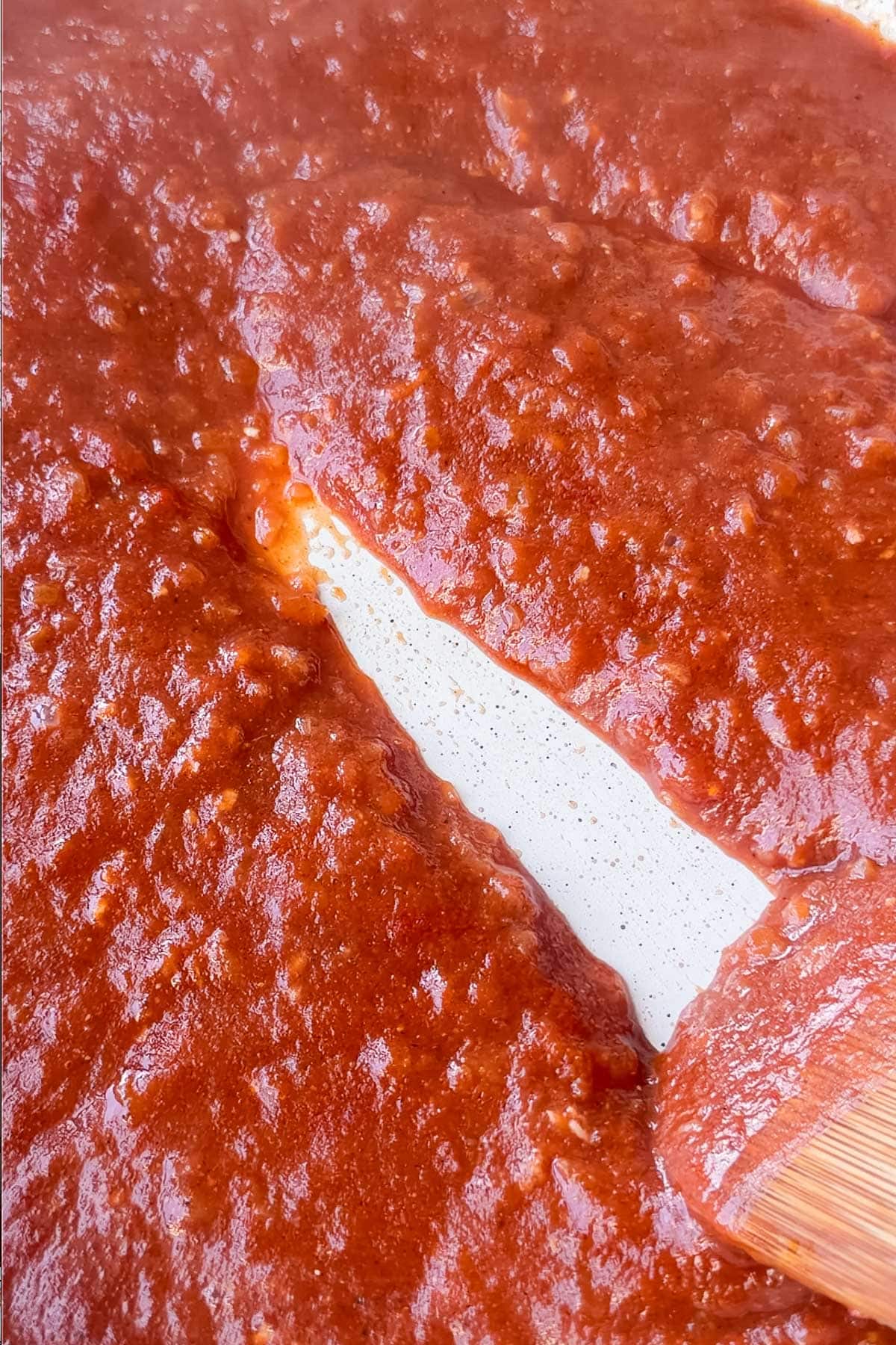 Thickened tomato sauce with a spoon trail across the skillet for butter chicken meatballs