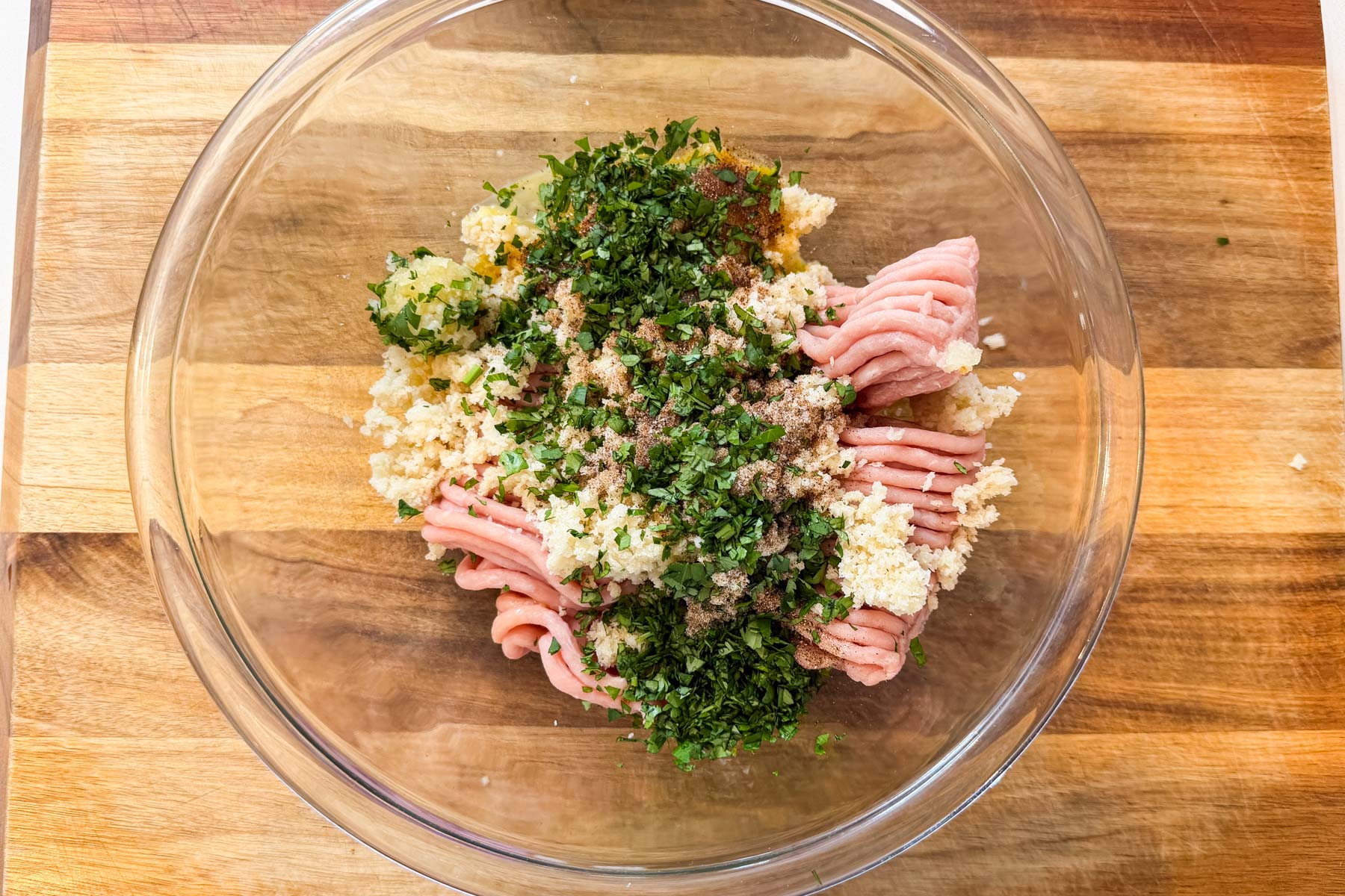 Ground chicken, cilantro, garlic, and spices in a glass bowl for butter chicken meatballs