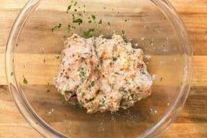 Mixed ground chicken meatball mixture with fresh cilantro in a glass bowl