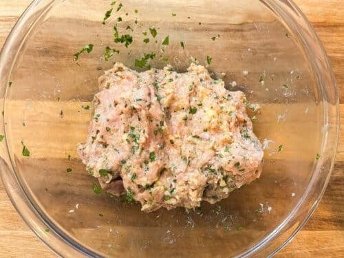 Mixed ground chicken meatball mixture with fresh cilantro in a glass bowl