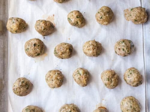 Rolled raw chicken meatballs lined up on a parchment-lined sheet pan