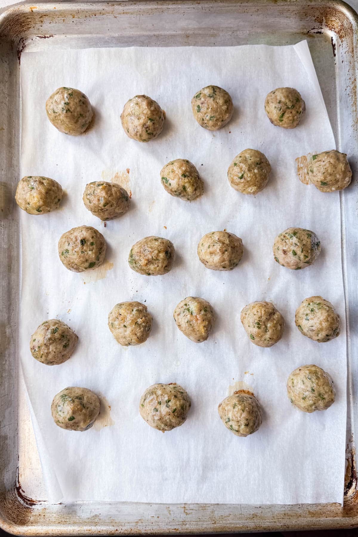 Rolled raw chicken meatballs lined up on a parchment-lined sheet pan