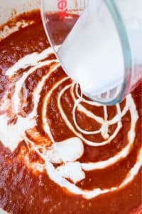 Heavy cream swirling into tomato sauce to make a creamy butter chicken sauce