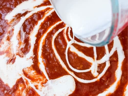 Heavy cream swirling into tomato sauce to make a creamy butter chicken sauce