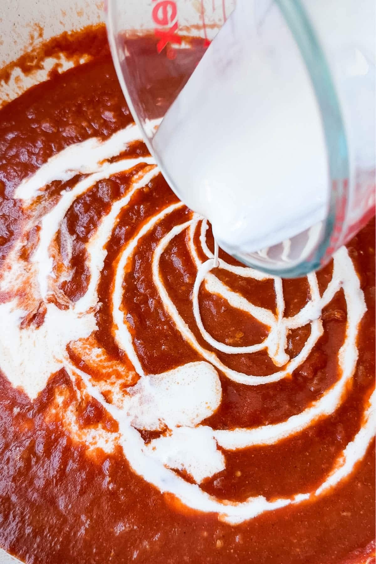 Heavy cream swirling into tomato sauce to make a creamy butter chicken sauce