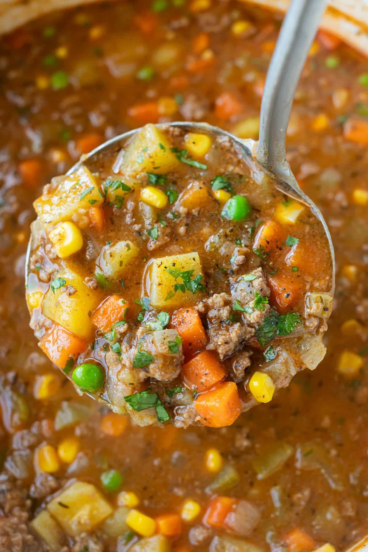 A ladle scoops up a big serving of shepherd's pie soup with ground beef, potatoes, corn, peas, and carrots.
