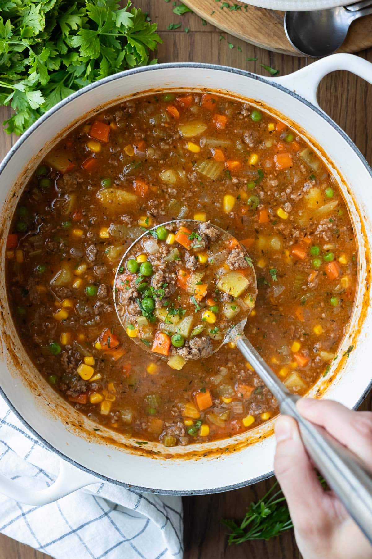 A ladle is scooping up some shepherd's pie soup with ground beef from a Dutch oven for dinner.