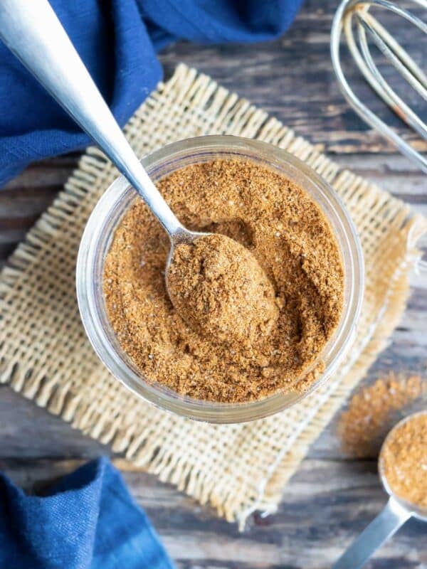 A spoon scooping homemade taco seasoning mix out of a glass jar.